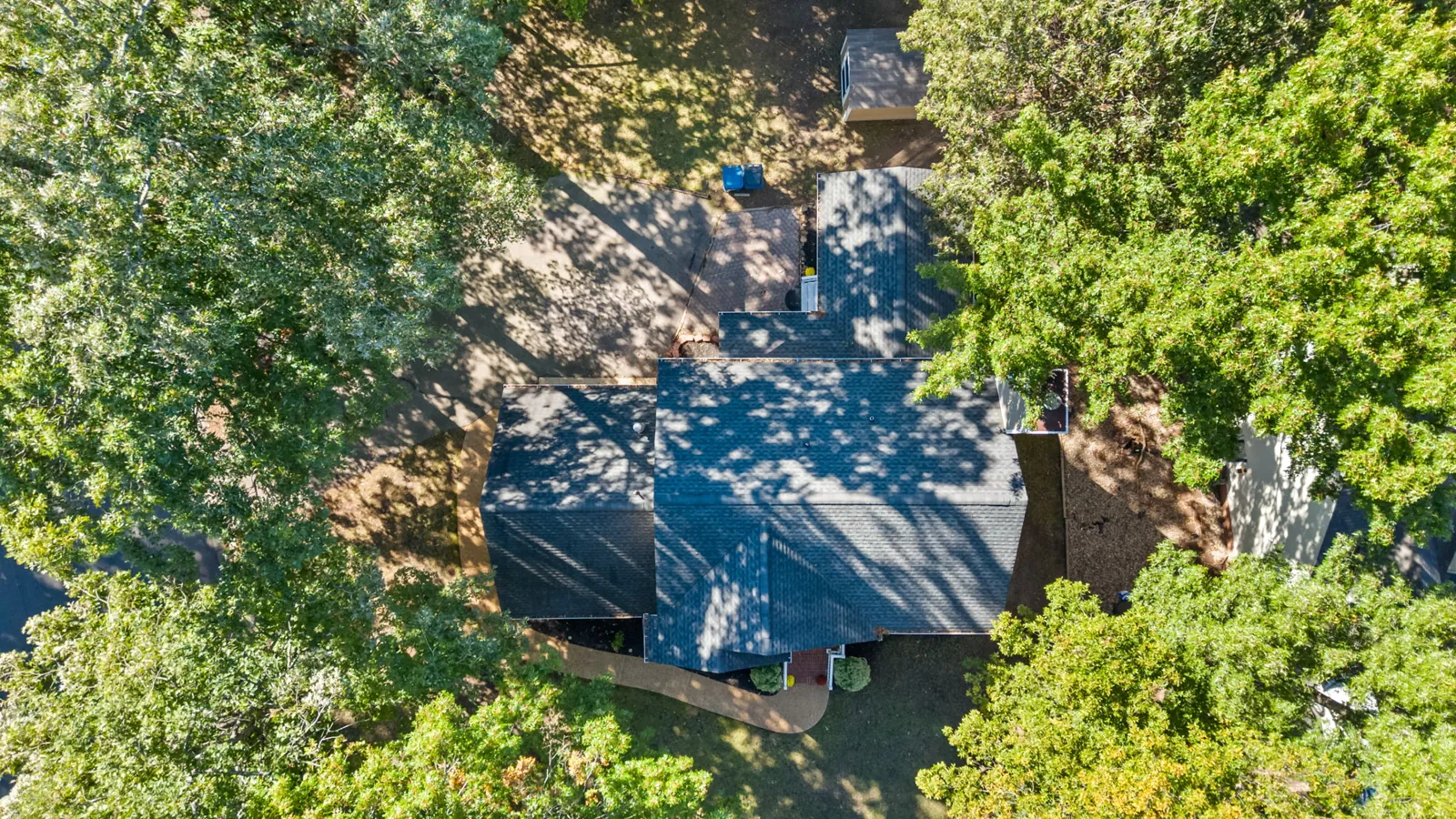 Aerial view of the home, driveway, and wooded lot with a backyard shed