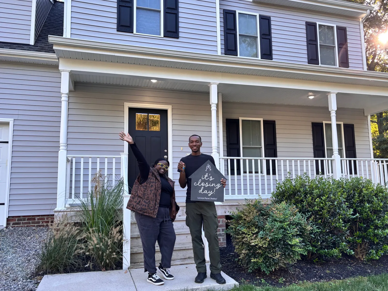 Happy couple holding keys and a closing day sign in front of their new home